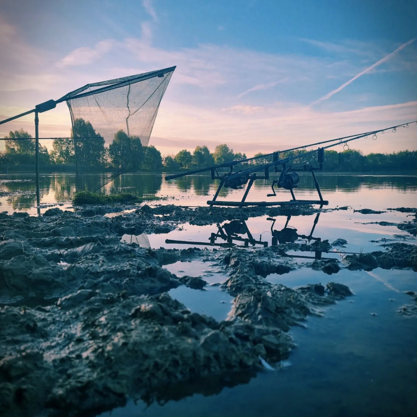 overlook of lake with carp rods and net on muddy ground with blue skies in the background