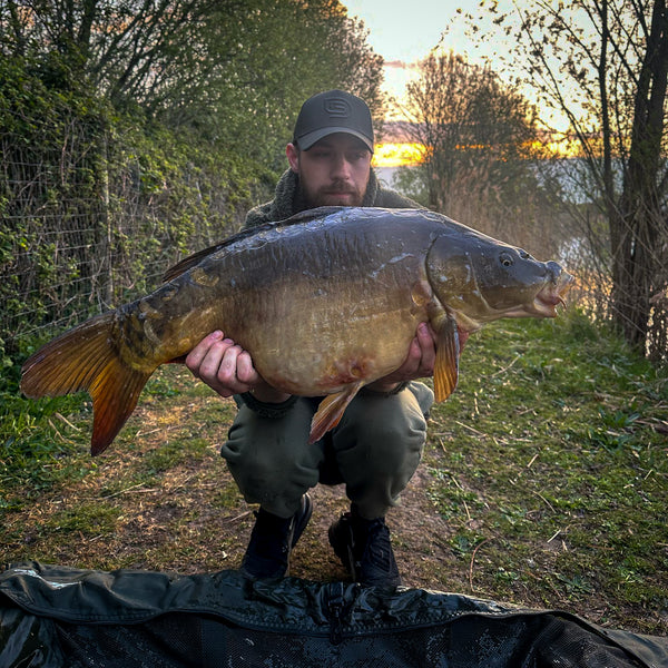 man holding mirror carp with carp lake and woods behind